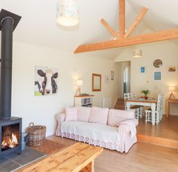 A living room with a wood stove next to a striped sofa and a dining table with white chairs at The Shippon at Wyke Farm in Lyme Regis