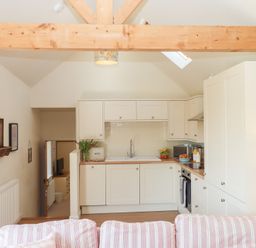 A kitchen with white cabinets and a sink with a striped sofa in front at The Shippon at Wyke Farm in Lyme Regis