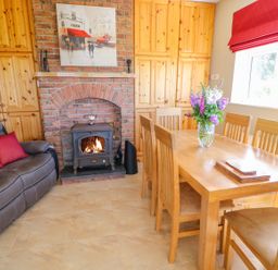 A dining room with a wooden table and chairs a leather sofa a brick fireplace and wooden cabinets at Sea View Hideaway in Lahinch County Clare