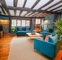 A living room with teal sofas wooden beams and a coffee table at 3 Masons Court in Stratford-Upon-Avon