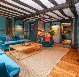 A living room with blue sofas and armchairs a wooden coffee table and exposed wooden beams at 3 Masons Court Stratford-Upon-Avon