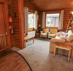 A sitting room with armchairs sofa wooden tables and windows in a wooden cabin at Glanton in Longframlington