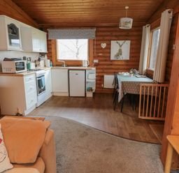 A kitchen and dining area with white cabinets a stove a small fridge a table with chairs and wooden walls at Glanton in Longframlington
