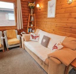 A living room with a beige sofa and two armchairs next to a wooden wall with a window and shelf at Glanton in Longframlington