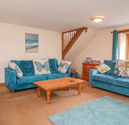 A living room with blue sofas floral and butterfly cushions wooden coffee table and wooden chest of drawers at The Shippon in Barnstaple
