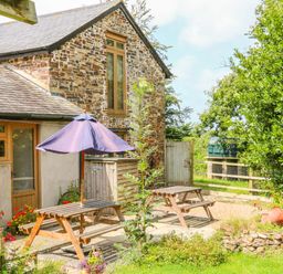 A stone cottage with wooden picnic tables and a purple umbrella in a garden at The Shippon in Barnstaple