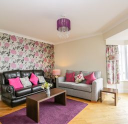 A living room with two sofas a wooden coffee table purple rug floral wallpaper and window with curtains at The Gansey Girl in Bridlington