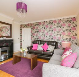 A living room with a dark brown sofa, a light gray sofa, a wooden coffee table, floral wallpaper, a purple rug, and a fireplace at The Gansey Girl in Bridlington