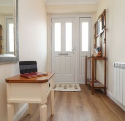 A hallway with a white side table holding a router and book and wooden coat rack near a white door at Tremethic in Trewoon