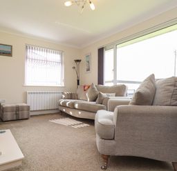 A living room with two beige sofas a wooden chair a window with vertical blinds and a purple vase on a shelf at Tremethic in Trewoon