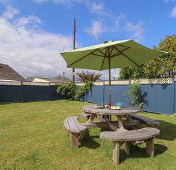 A garden with a round wooden picnic table and green umbrella at Tremethic in Trewoon