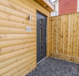 An exterior entrance with a black door next to a wooden wall with a sign reading Cilan Lodge at Llandrillo