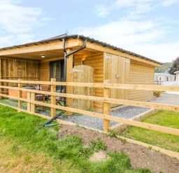 A wooden cabin with a covered porch and outdoor seating behind a wooden fence at Cilan Lodge in Llandrillo