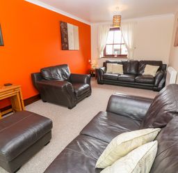 A living room with brown leather sofas and an orange accent wall at Mossley Cottage in St Buryan