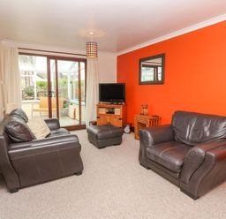 A living room with two leather sofas an ottoman a wooden tv stand with a television and a small wooden side table at Mossley Cottage in St Buryan