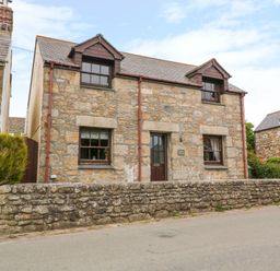 Stone house with two dormer windows and a stone wall in front at Mossley Cottage in St Buryan