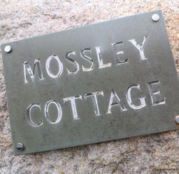 A metal sign with the text mossley cottage mounted on a stone wall at Mossley Cottage in St Buryan