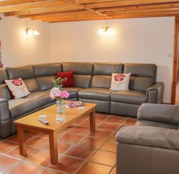 A living room with a gray sectional sofa and armchair a wooden coffee table with flowers and magazines on tile floor at Conquer Hall in Hendomen near Montgomery
