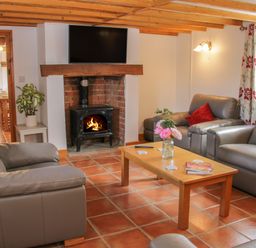 A living room with leather sofas a wooden coffee table a fireplace with a fire and a television mounted above at Conquer Hall in Hendomen near Montgomery