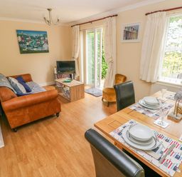A living and dining area with a brown sofa a wooden dining table set for four and sliding glass doors at 2 Primrose Cottage Saundersfoot