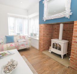 A living room with a patchwork sofa white wood stove in a red brick fireplace and a white coffee table at Waterside in Beadnell