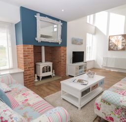A living room with patterned sofas a white coffee table a wood stove in a brick fireplace and a TV at Waterside in Beadnell