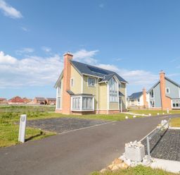 A residential street with detached houses and driveways under a blue sky at Waterside in Beadnell