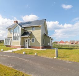 A detached two-story house with a front lawn and solar panels on the roof at Waterside in Beadnell
