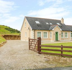A detached house with a green front door surrounded by a gravel driveway and a wooden gate at Croghan in Portsalon