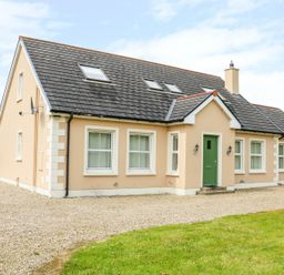A beige house with a green door and multiple windows surrounded by gravel and grass at Croghan in Portsalon
