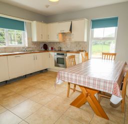 A kitchen with cream cabinets a wooden dining table with chairs and windows with blue blinds at Croghan in Portsalon