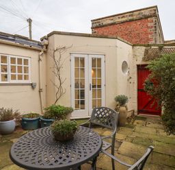 A small courtyard with a metal table and chairs several potted plants and a red door at 20A St Hilda's Whitby