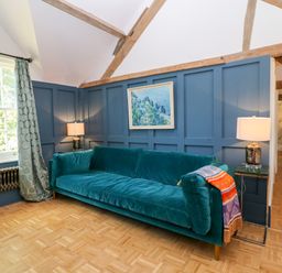 A room with a teal sofa blue paneled walls wooden beams two lamps a window with patterned curtains and a parquet floor at The Hemmel in Faringdon