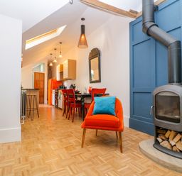 A kitchen and dining area with a wood-burning stove and orange chair at The Hemmel in Faringdon