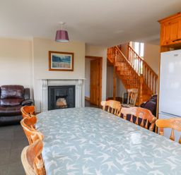A dining table with wooden chairs a leather sofa a fireplace wooden stairs and a refrigerator at Doornogue Churchtown near Fethard-on-Sea