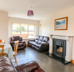 A living room with brown leather sofas a dining table with chairs and a fireplace with a painting above it at Doornogue in Churchtown near Fethard-on-Sea