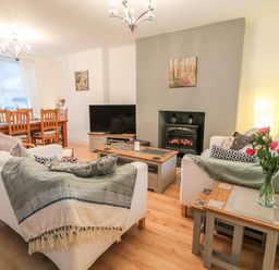 A living room with two white sofas a coffee table a television and a dining table with chairs at Yr Adfa The Retreat in Blaenau Ffestiniog