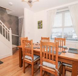 A dining room with a wooden table and six chairs near a window with white curtains at Yr Adfa The Retreat in Blaenau Ffestiniog