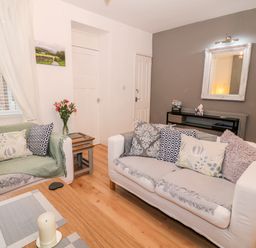 A living room with two sofas pillows a wooden coffee table with candle flowers on a side table and a mirror on the wall at Yr Adfa The Retreat in Blaenau Ffestiniog