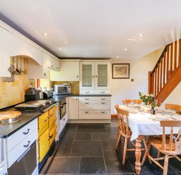 A kitchen with white cabinets yellow appliances a dining table set with plates and glasses and wooden stairs at Great Bradley Cottage in Withypool