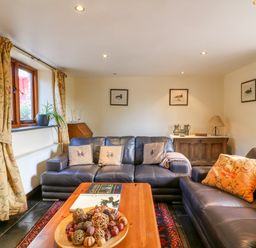 A living room with leather sofas a wooden coffee table with decorative bowl a sideboard with a lamp and framed pictures on the wall at Great Bradley Cottage in Withypool