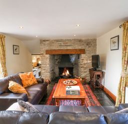 A living room with leather sofas a wooden coffee table a stone fireplace and a television at Great Bradley Cottage in Withypool