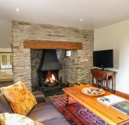 A living room with a stone fireplace and a wooden coffee table with books and decorative items at Great Bradley Cottage in Withypool