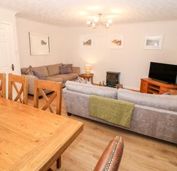 A living room with two sofas a wooden dining table chairs a television and a small stove at 4 Ty Rhosyn in Morfa Bychan