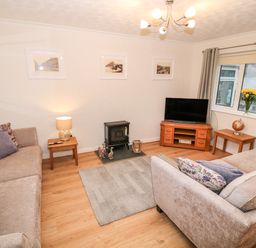 A living room with two sofas a TV on a stand a small stove and framed pictures on the wall at 4 Ty Rhosyn Morfa Bychan