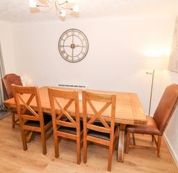A dining room with a wooden table surrounded by six chairs a wall clock and a floor lamp at 4 Ty Rhosyn Morfa Bychan