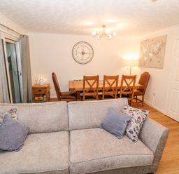 A living area with a gray sofa and a wooden dining table with chairs at 4 Ty Rhosyn in Morfa Bychan