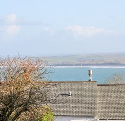 A view of rooftops and trees with the sea and hills in the background at Driftwood Haven in Carbis Bay