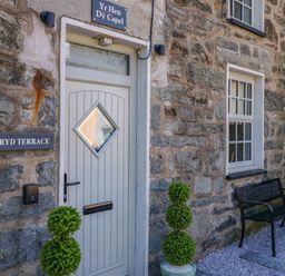 The stone exterior of a building with a white door and a bench outside at Yr Hen Dy Capel in Blaenau Ffestiniog