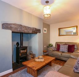 A living room with leather sofas a wooden coffee table a wood burning stove and a floor lamp at Yr Hen Dy Capel in Blaenau Ffestiniog